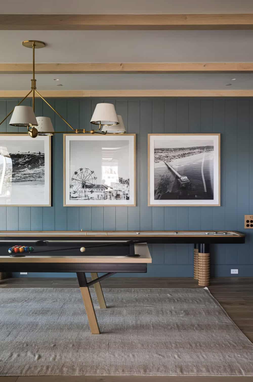 Game room with shuffleboard table, dusty blue shiplap walls, brass chandelier, and black-and-white coastal photography