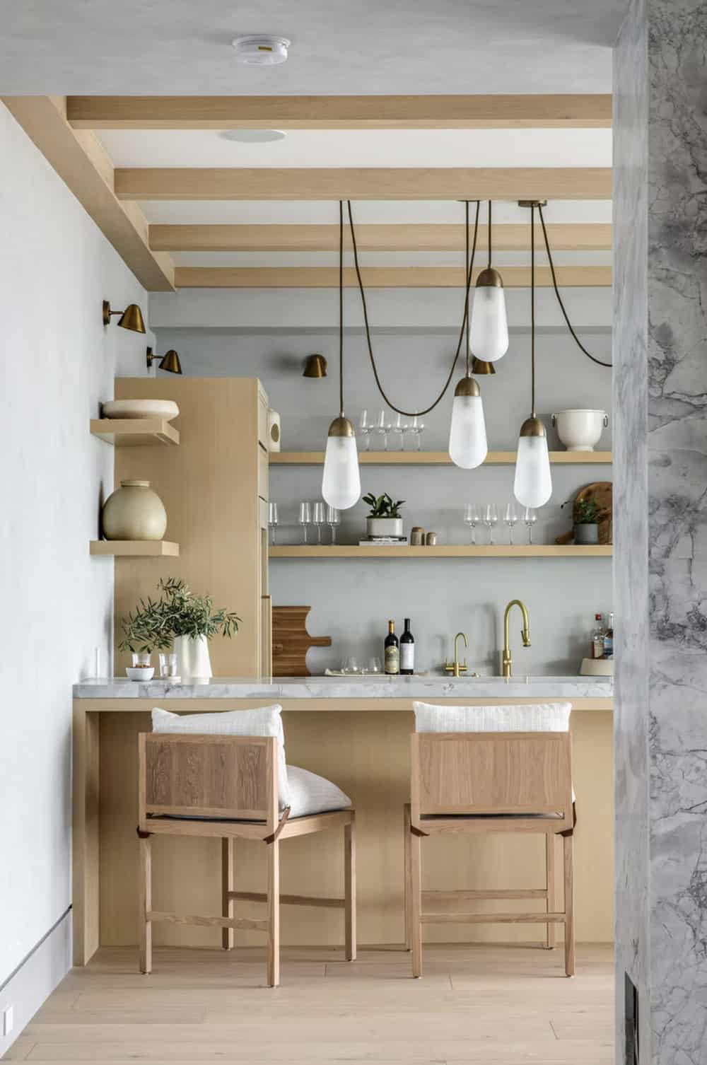 Wet bar niche with marble countertop, brass faucet, open shelving, and frosted glass pendant lights