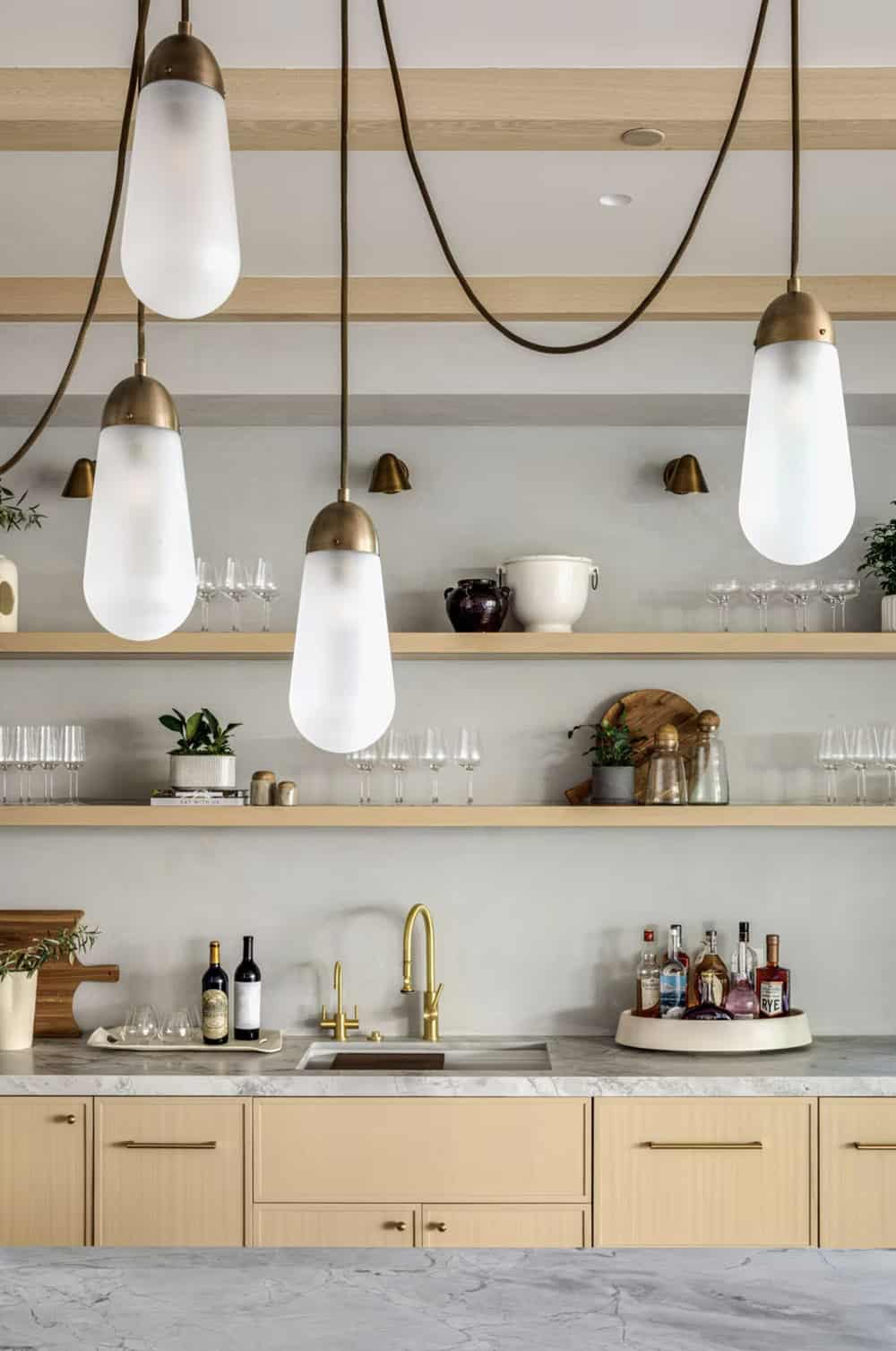 Bar area detail with frosted glass pendant cluster, brass hardware, open shelving, and marble countertop