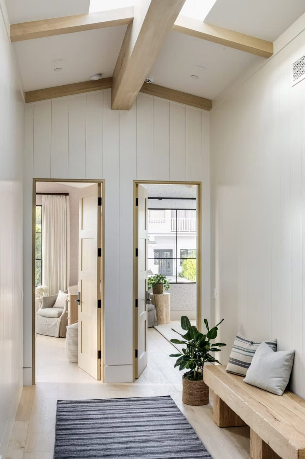 Upper-level hallway with vaulted beamed ceiling, shiplap wall, skylights, and raw wood bench