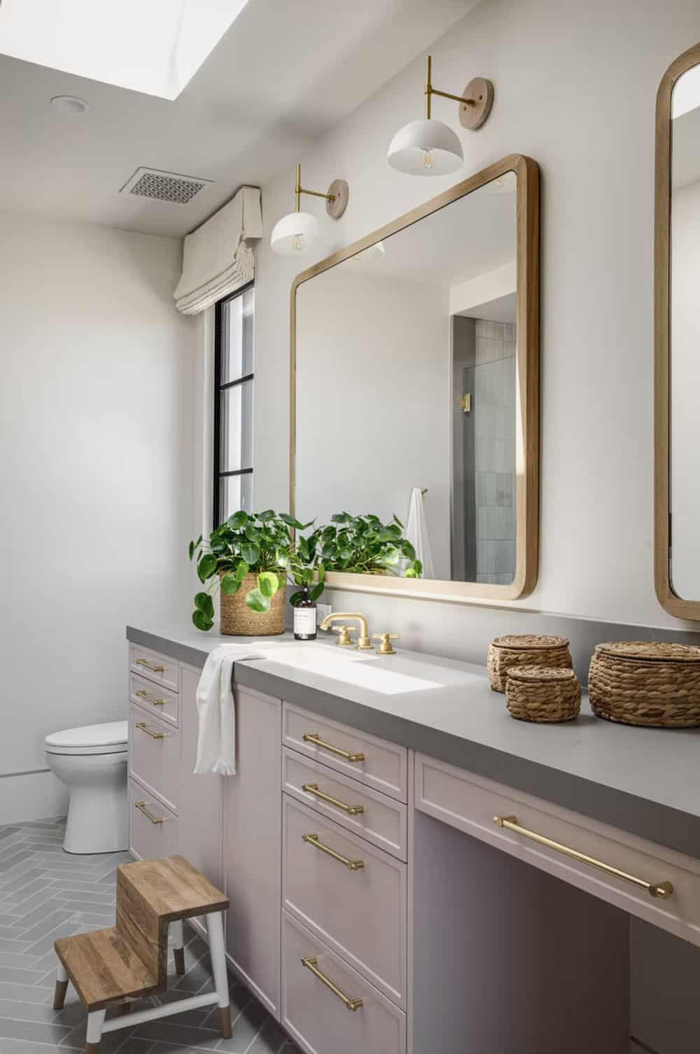 Kids' bathroom with blush-pink cabinetry, brass hardware, wood-framed mirrors, and herringbone tile floor