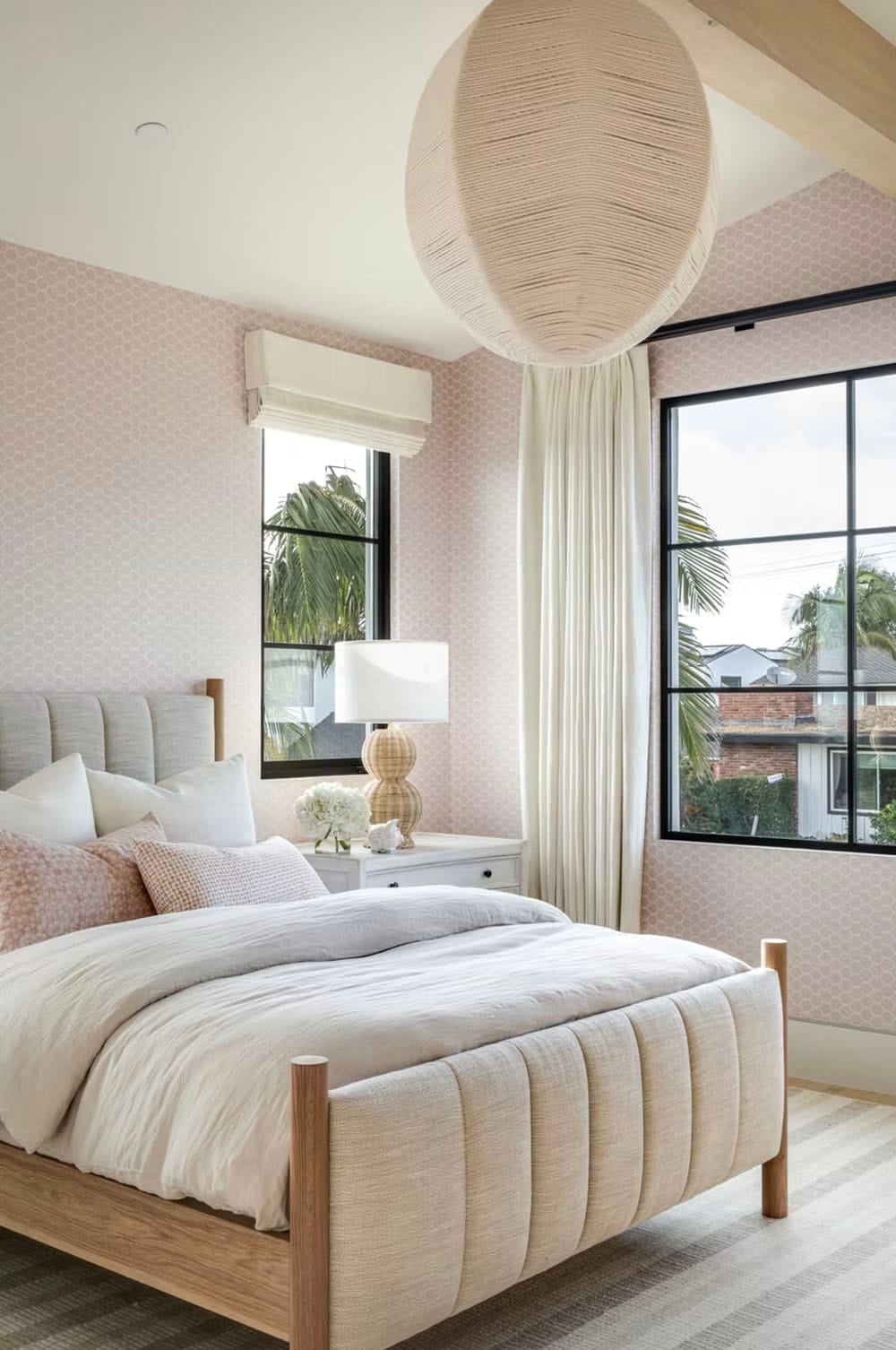 Guest bedroom with pink patterned wallpaper, upholstered channel-tufted bed, and round woven pendant light