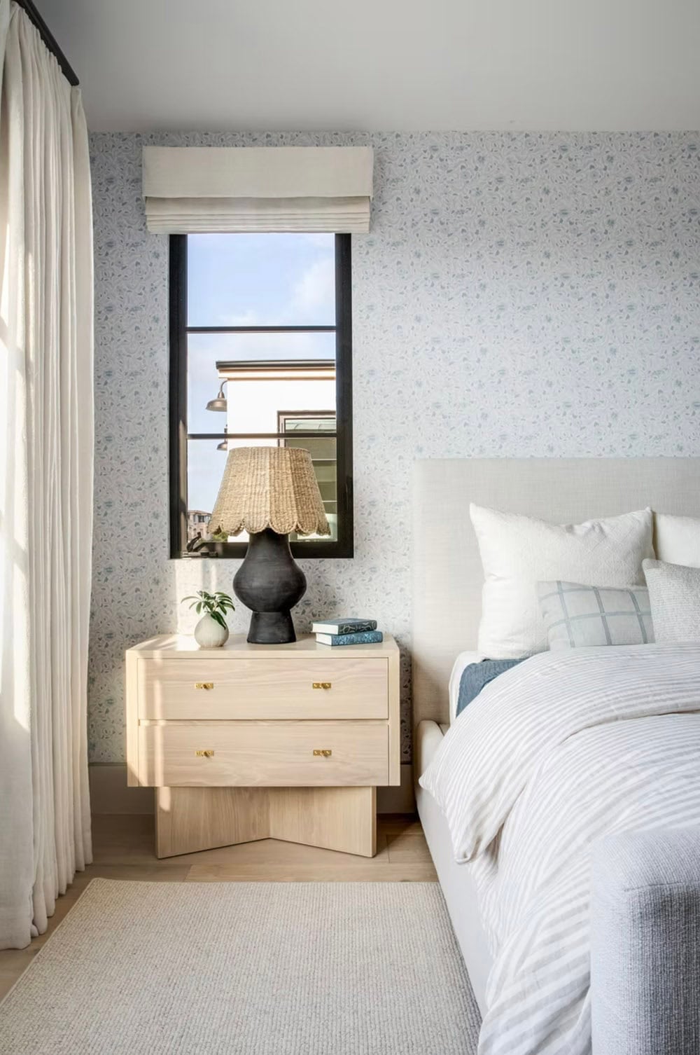 Guest bedroom nightstand with sculptural black lamp, light oak drawer chest, and delicate floral wallpaper