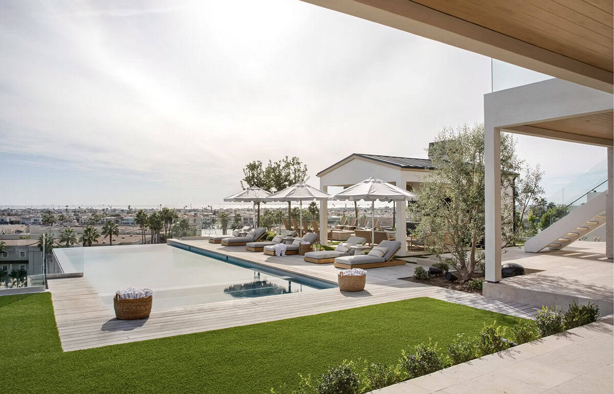 Infinity pool and sun deck with lounge chairs, striped umbrellas, lawn, and sweeping coastal views