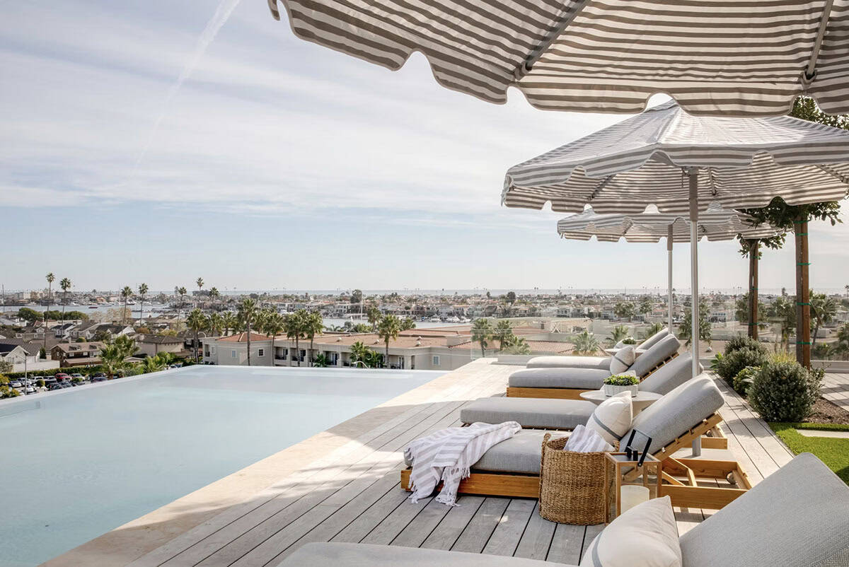 Infinity pool edge with teak chaises, striped umbrellas, and unobstructed harbor and ocean views