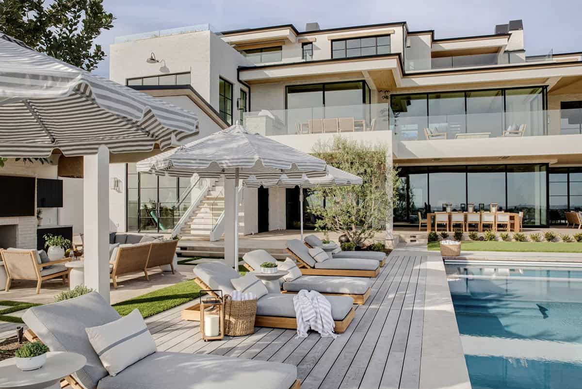 Rear exterior of coastal home with pool deck, multiple terraces, glass railings, and black-framed windows