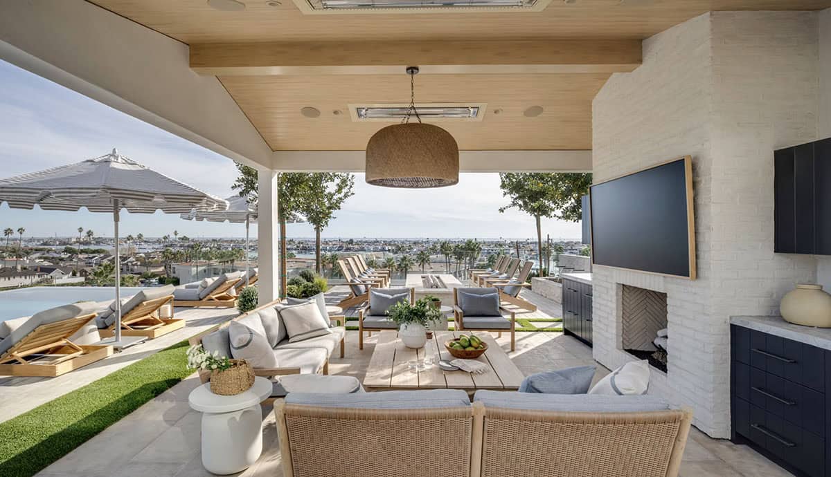 Outdoor cabana seating area with rattan pendant, fireplace, teak furniture, and panoramic harbor views