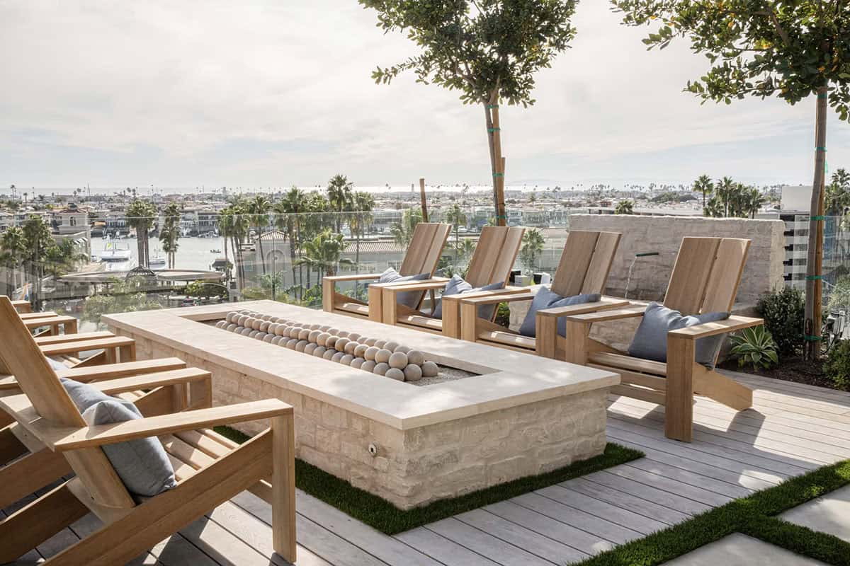 Close-up of stone fire pit with ceramic ball detail, teak lounge chairs, and harbor views