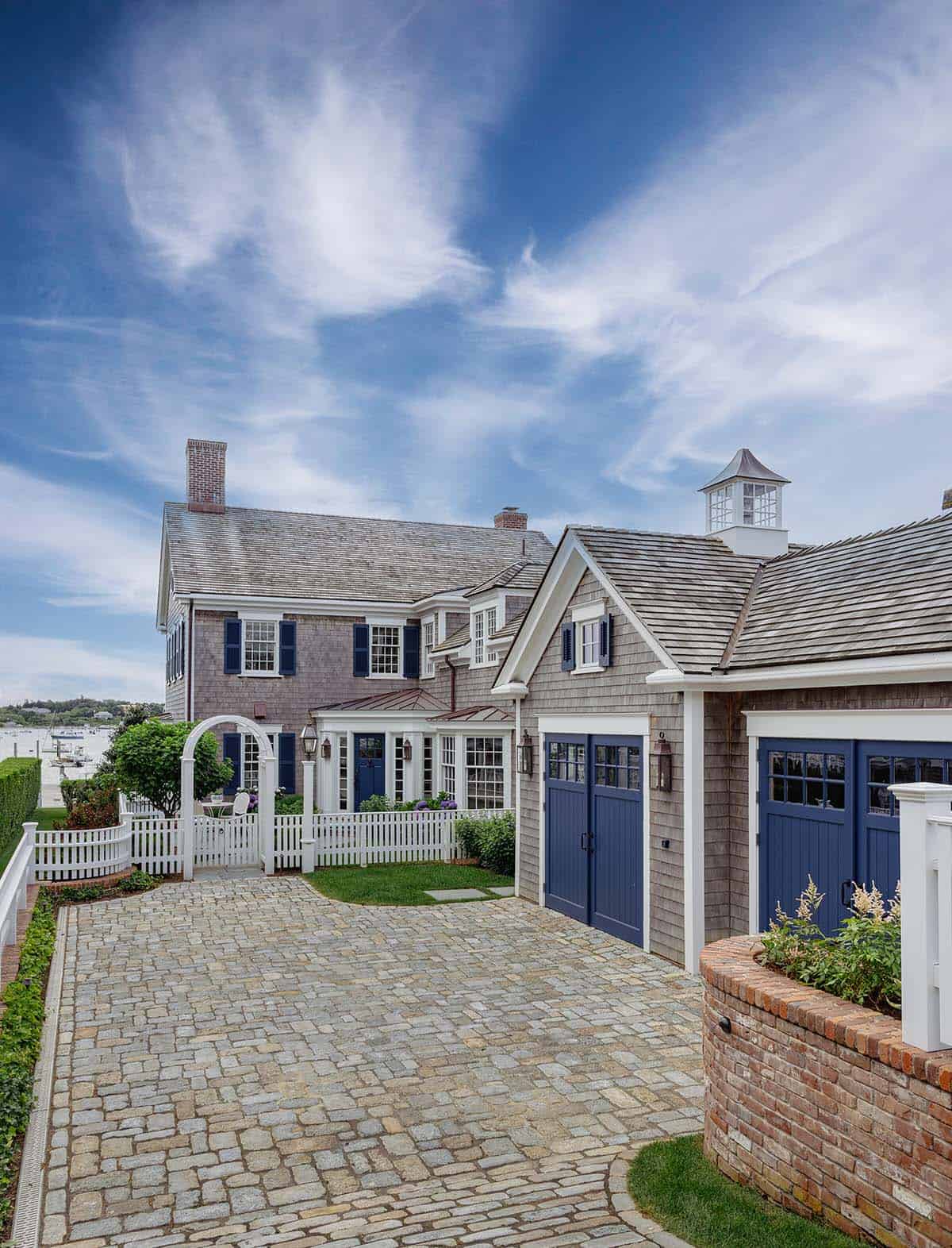 Colonial revival shingle-style home with navy garage doors and cobblestone driveway
