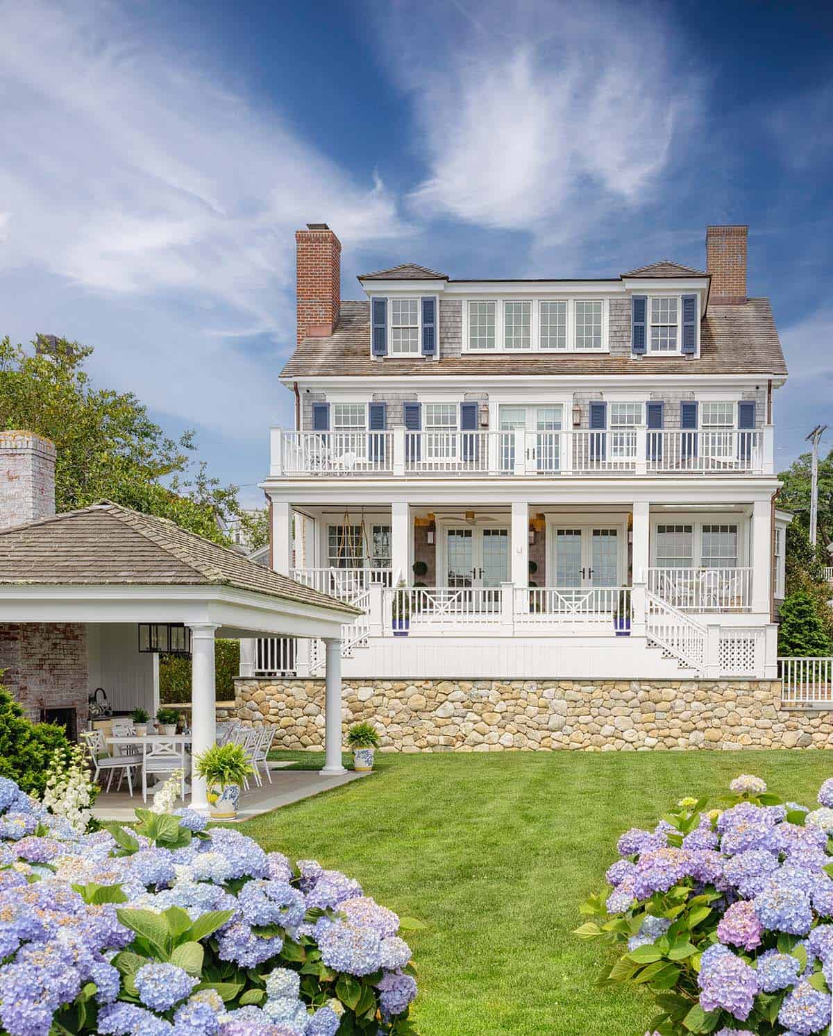 Three-story colonial revival coastal home with wraparound porch and hydrangea garden