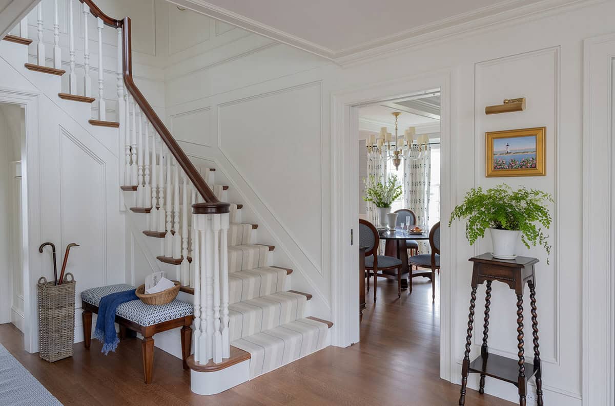Classic white foyer with spindle staircase, striped carpet runner and wainscoting