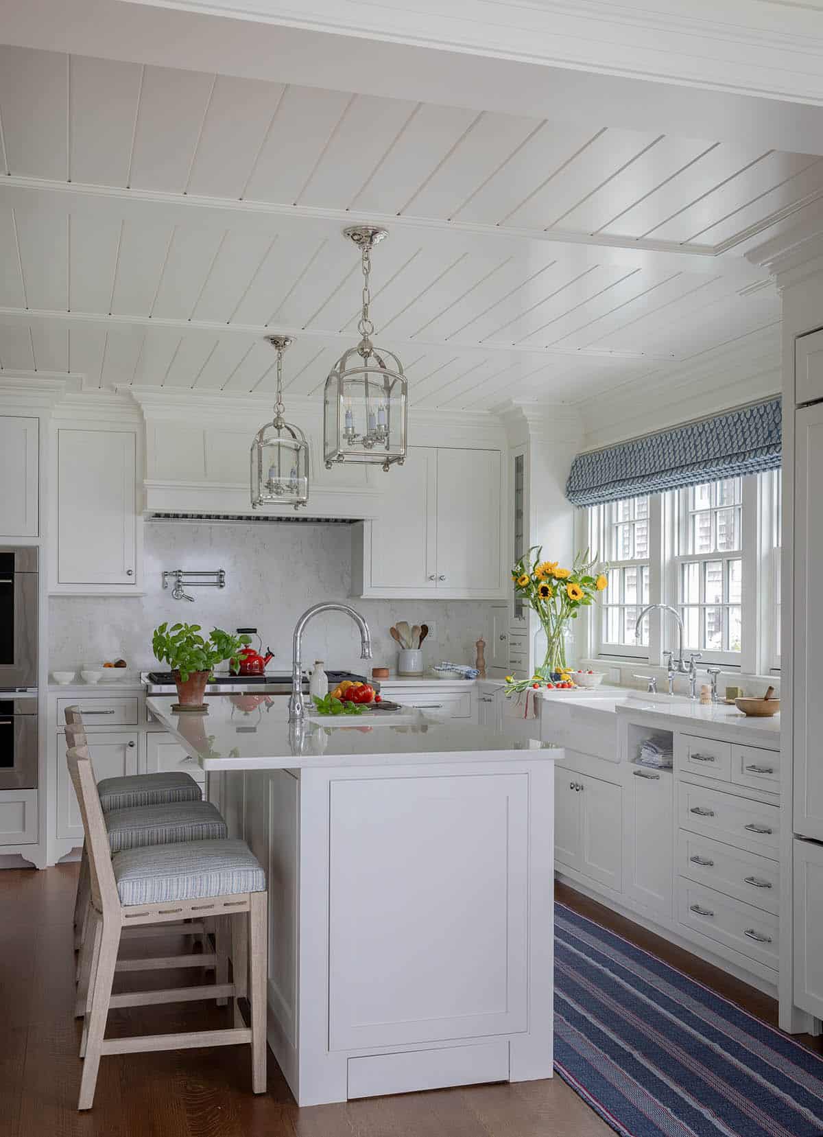 White kitchen with shiplap ceiling, lantern pendants, island and farmhouse sink