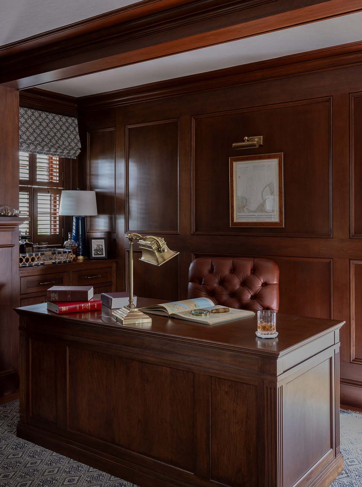 Dark walnut wood-paneled home office with tufted leather chair and brass desk lamp