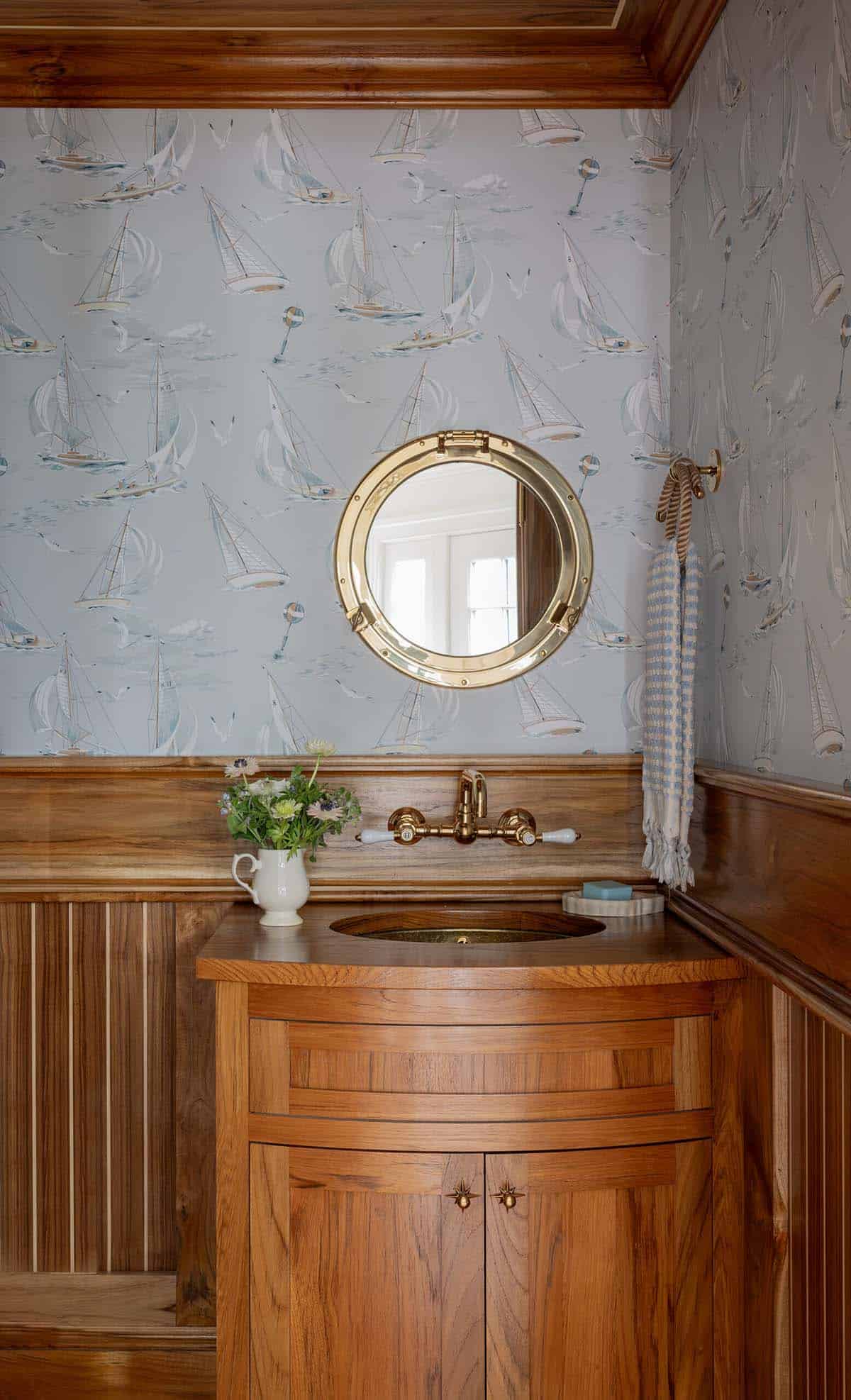 Powder room with sailboat wallpaper, porthole mirror and curved teak vanity