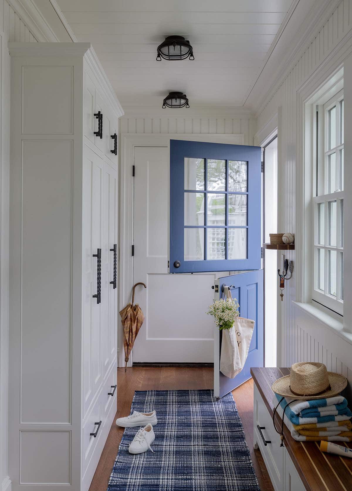 White beadboard mudroom with blue Dutch door and nautical cage ceiling lights