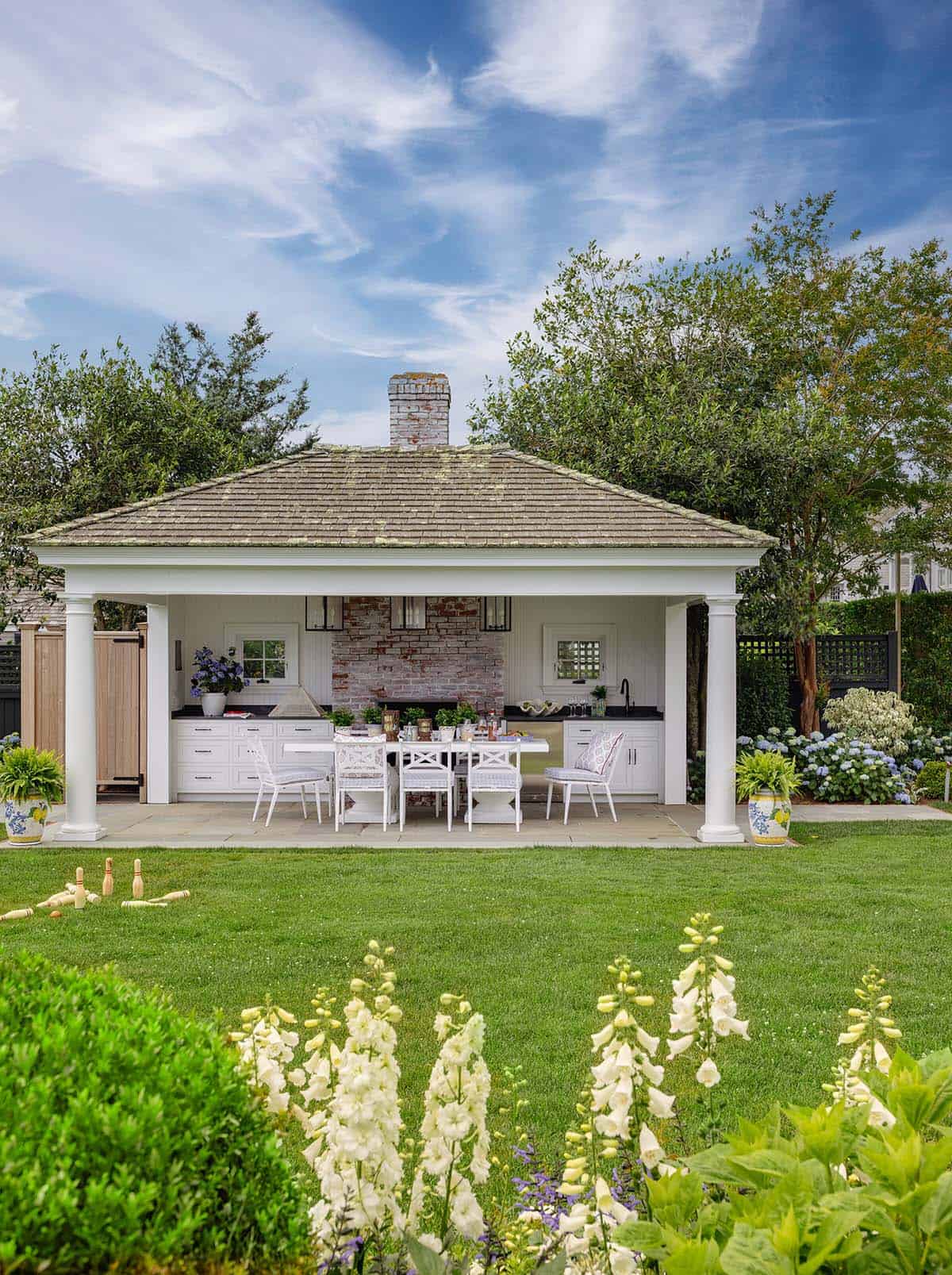 Outdoor kitchen pavilion with brick fireplace, white columns and perennial garden
