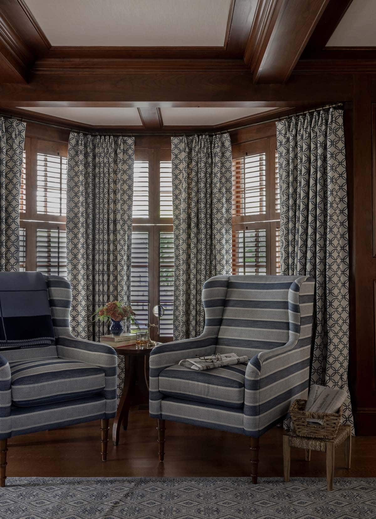 Dark wood-paneled study with bay window, striped wingback chairs and coffered ceiling
