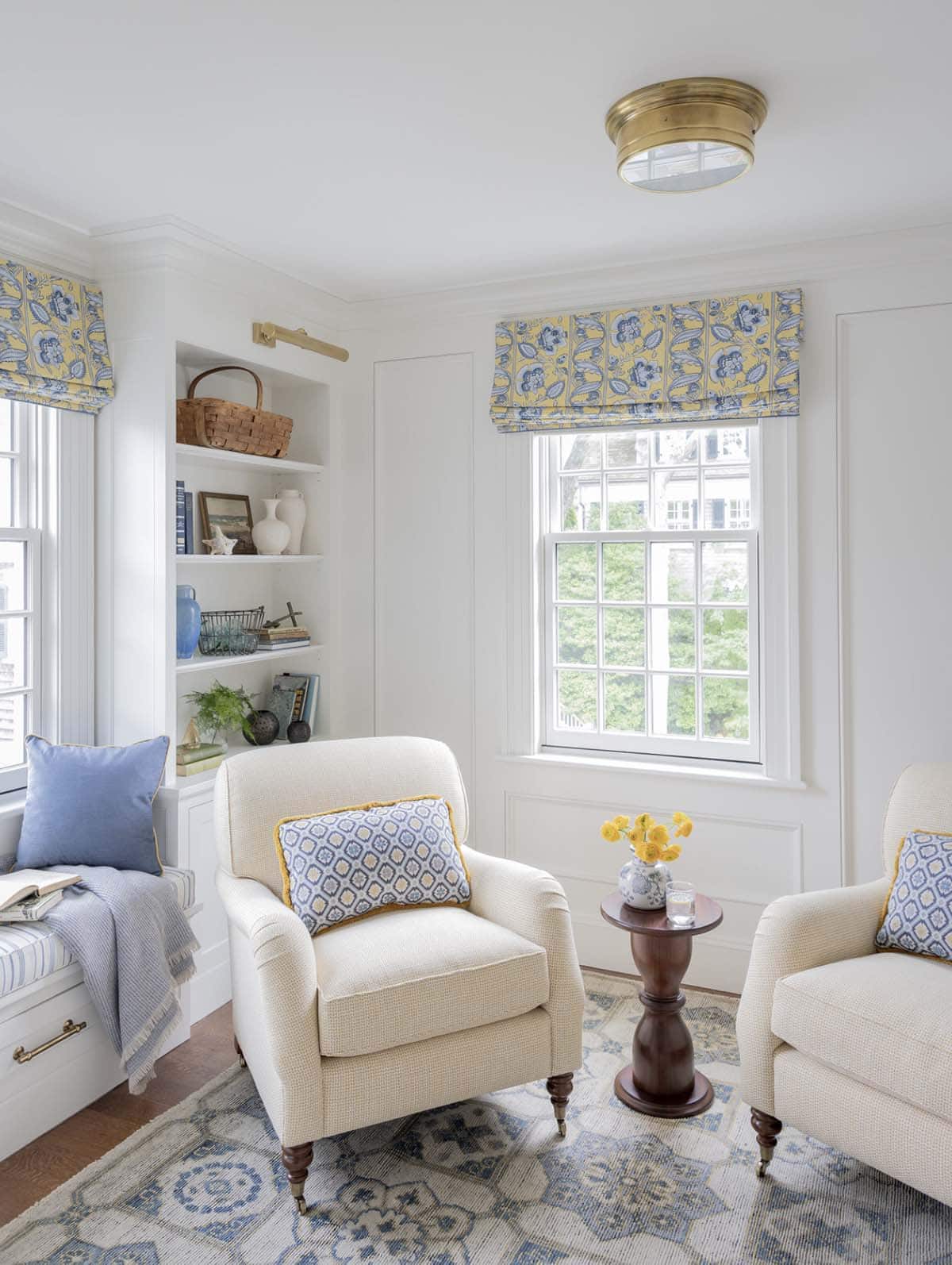 Bright sitting room with cream armchairs, yellow floral roman shades and built-in bookshelves