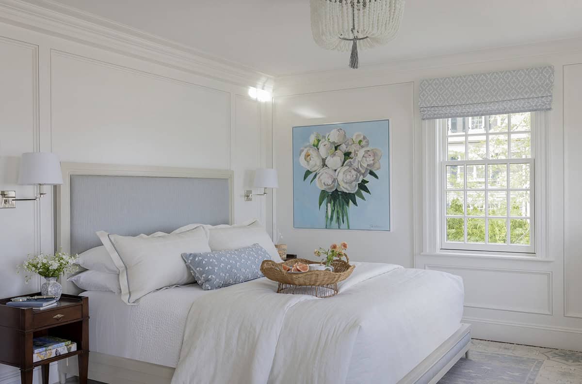 Primary bedroom with pale blue upholstered headboard, white wainscoting and peony floral painting