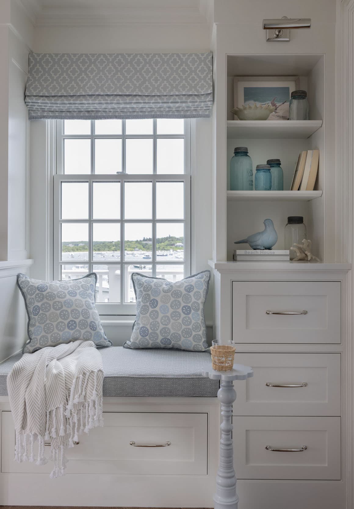 Harbor-view window seat with sand dollar pillows, built-in drawers and coastal shelf decor