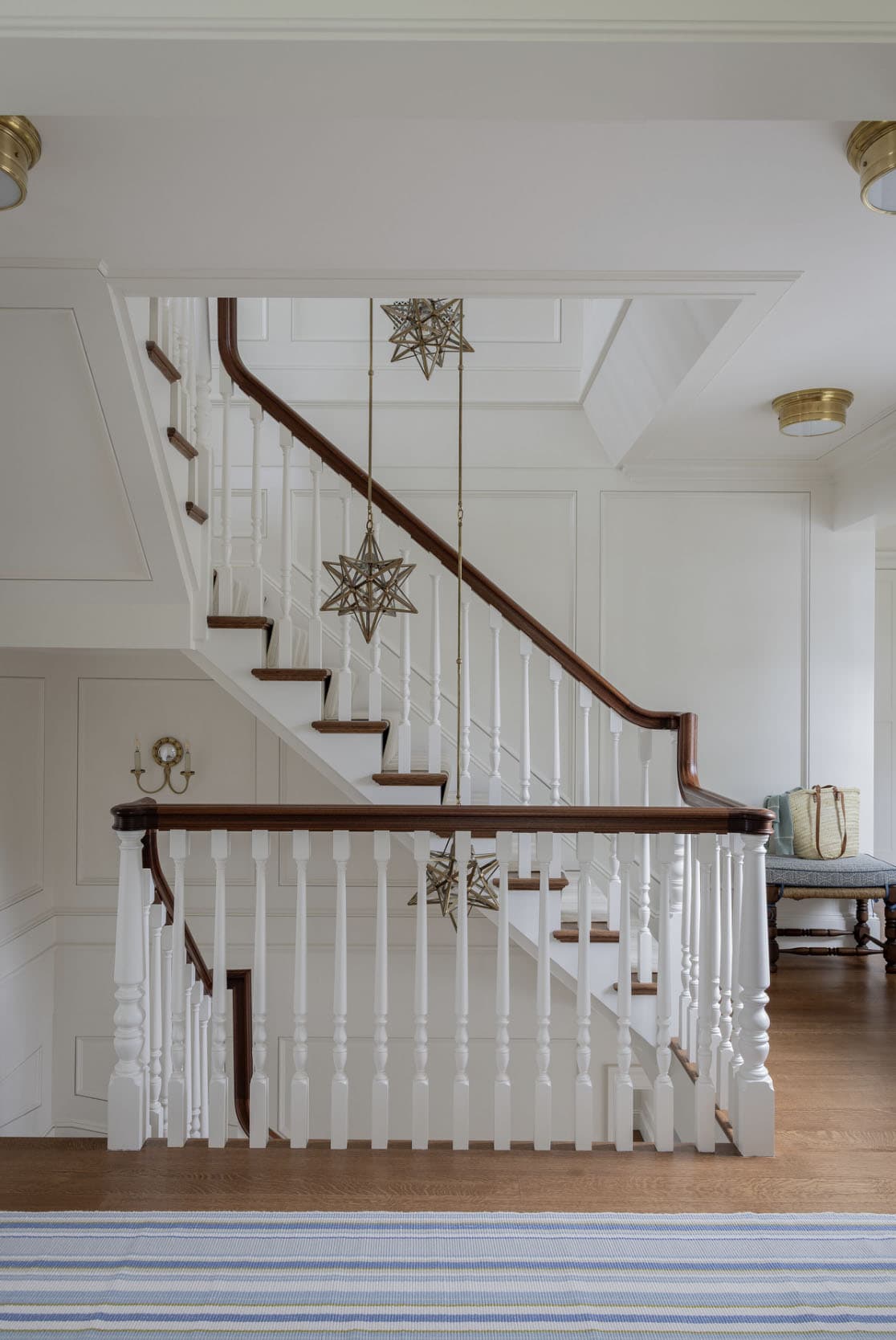 White staircase hall with walnut handrail, Moravian star pendant lights and wainscoting