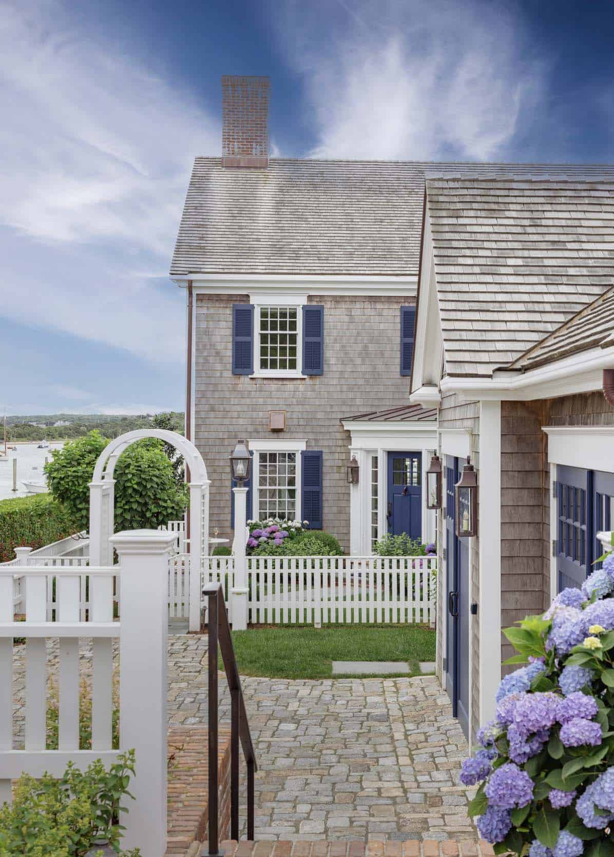 Shingle-style coastal home exterior with navy shutters, cobblestone path and hydrangeas