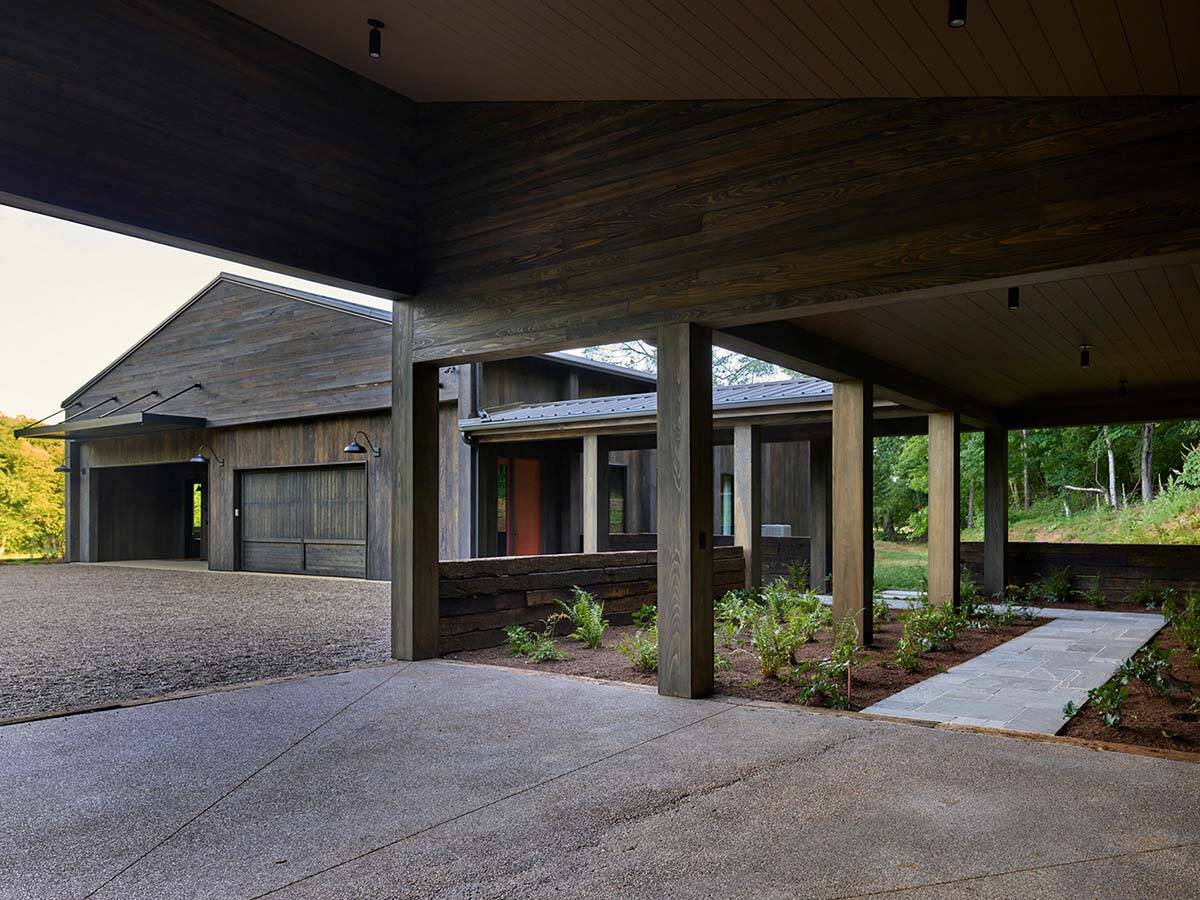 Covered porte-cochère with dark wood ceiling, timber columns, gravel driveway, and stone entry path