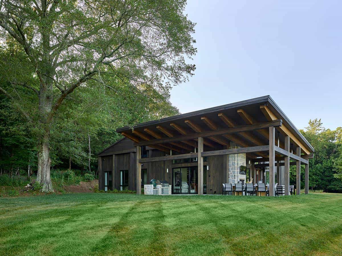 Rear view of contemporary farmhouse with large timber pergola, outdoor kitchen, dining area, and rolling lawn