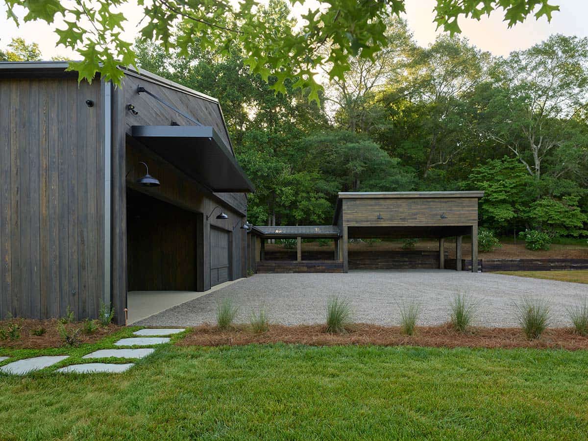 Dusk view of garage wing and separate carport structure with gravel courtyard and ornamental grasses
