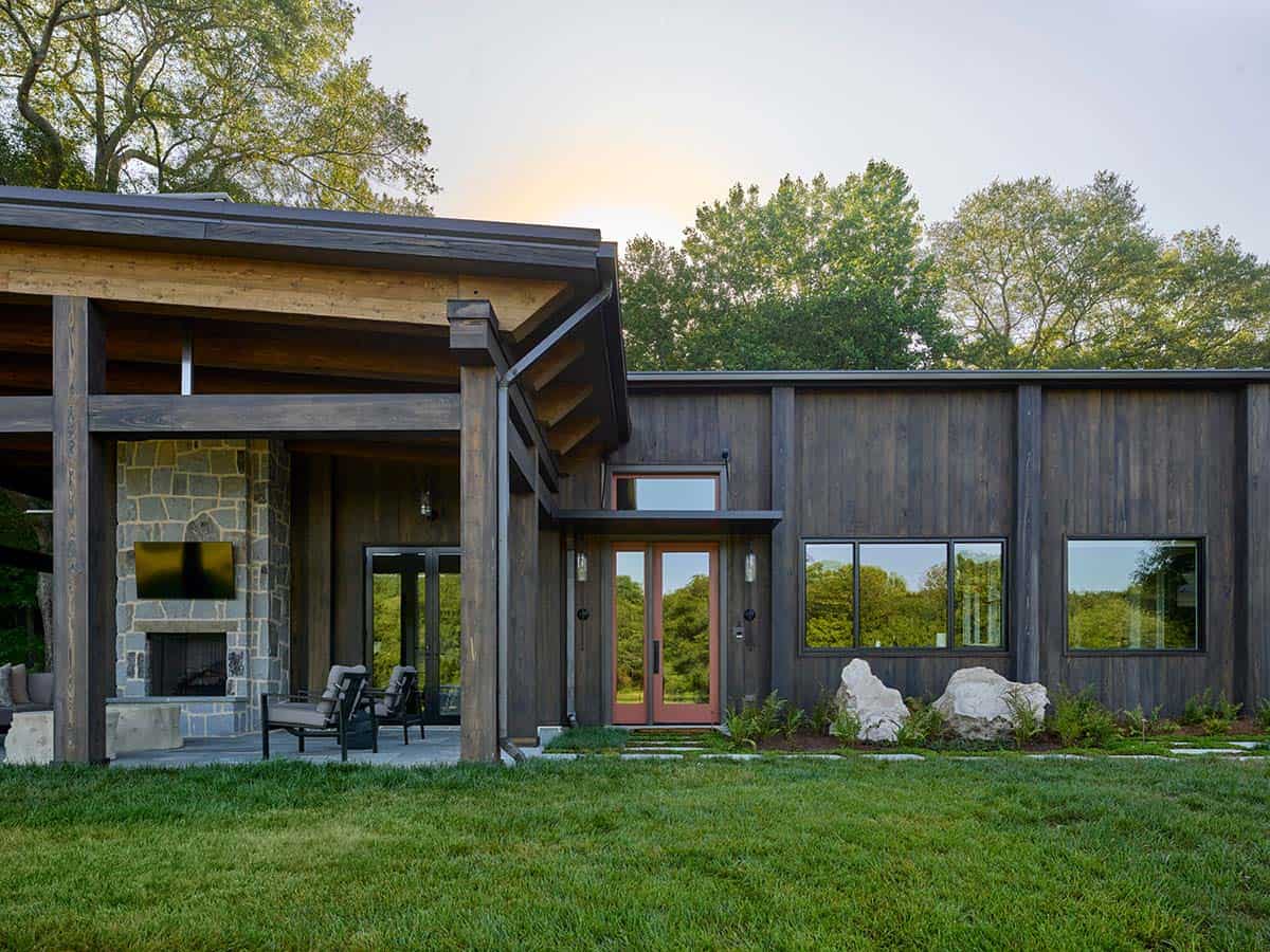 Close-up of contemporary barn home entry with red French doors, stone fireplace, and timber roof structure