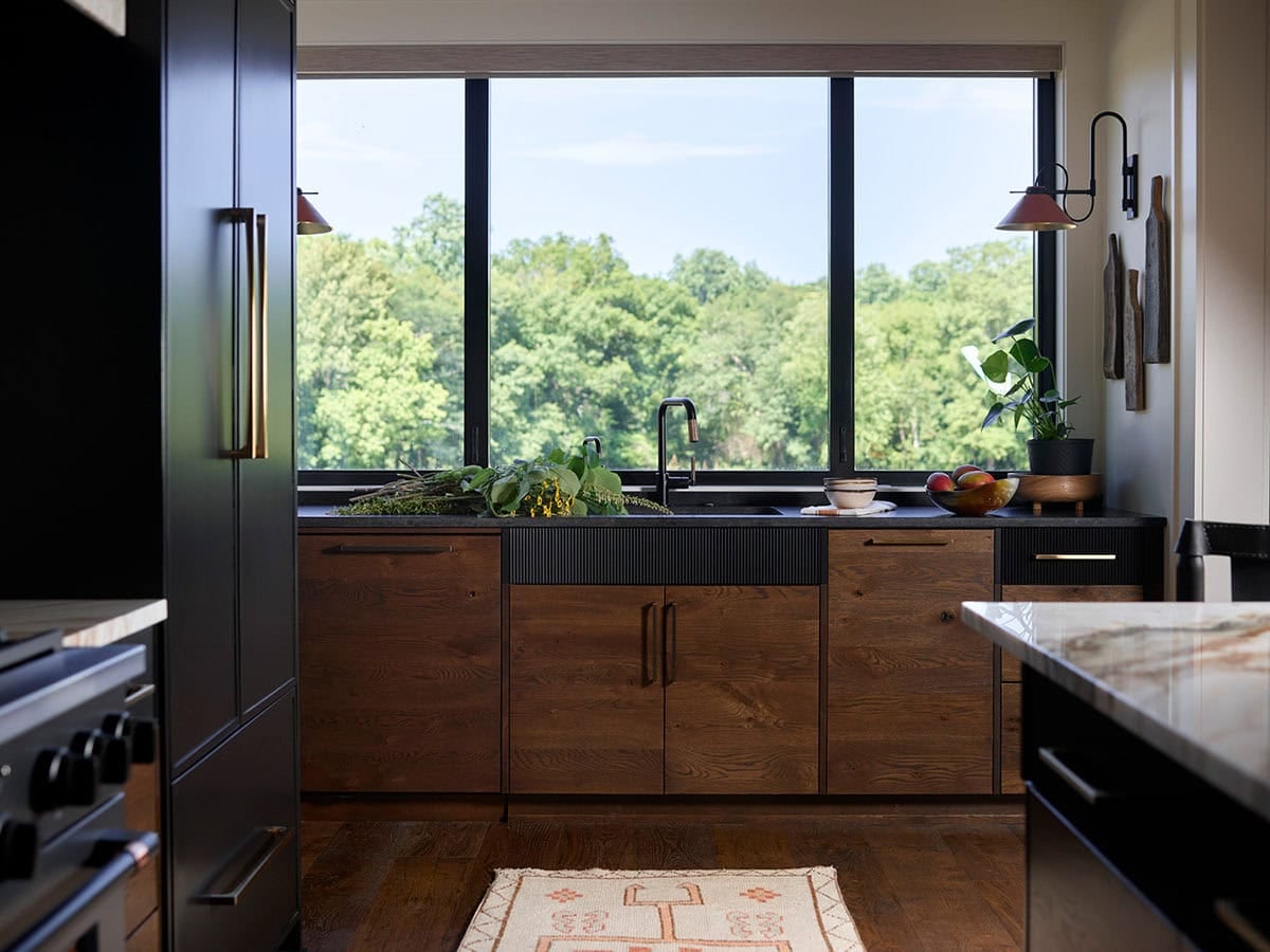 Dark walnut kitchen cabinets with black countertops and large picture window overlooking trees