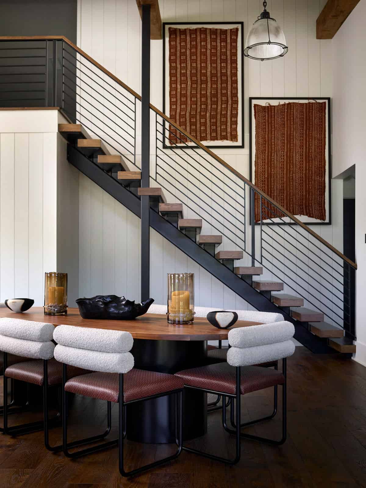 Floating wood staircase with black metal railings beside oval dining table and boucle chairs