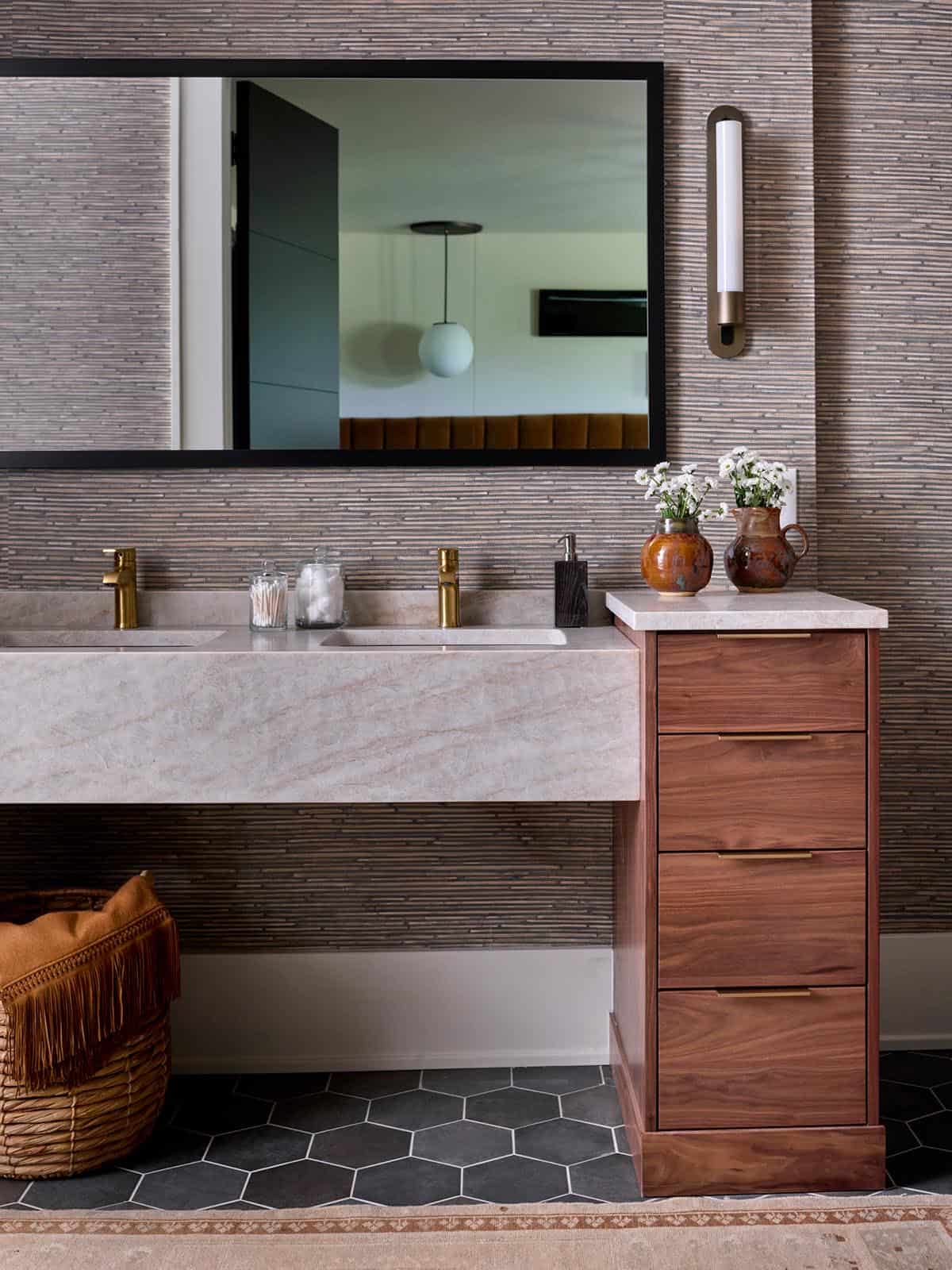 Primary bathroom double vanity with pink marble countertop, walnut drawers, and grasscloth walls