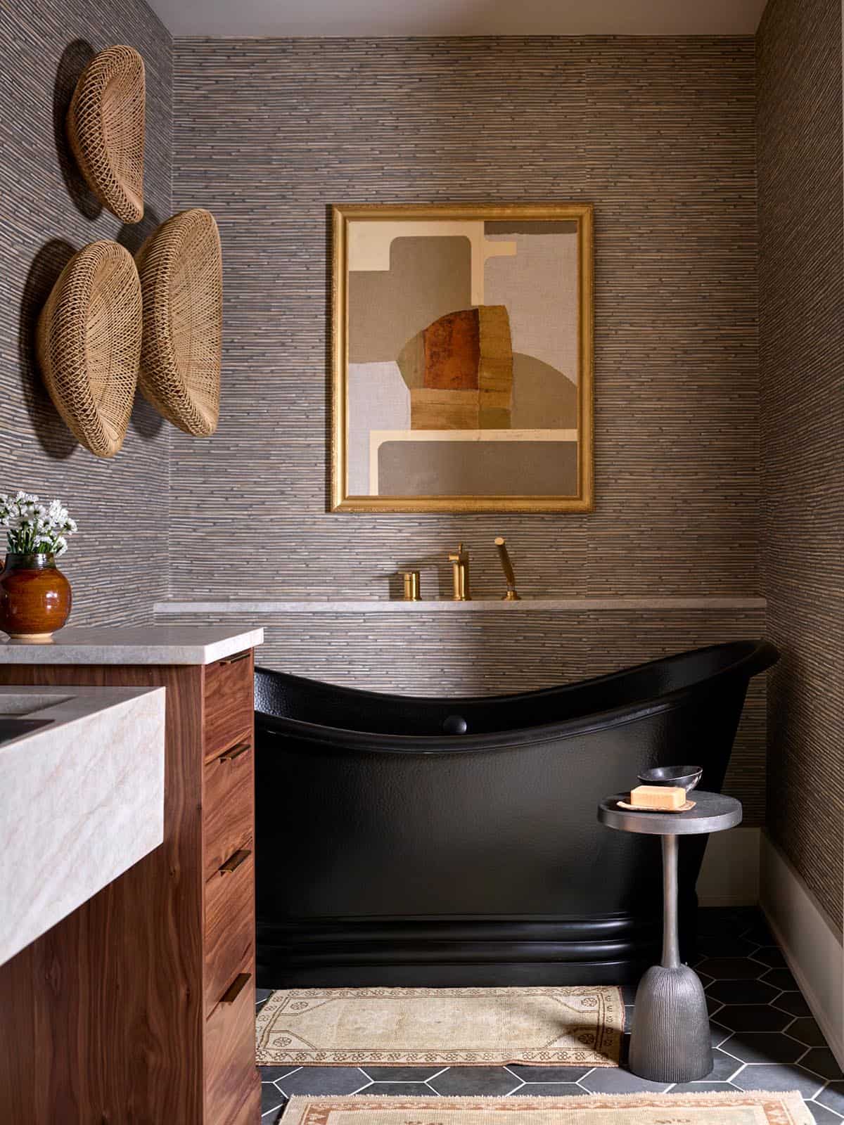 Freestanding matte black soaking tub with brass fixtures and abstract art above