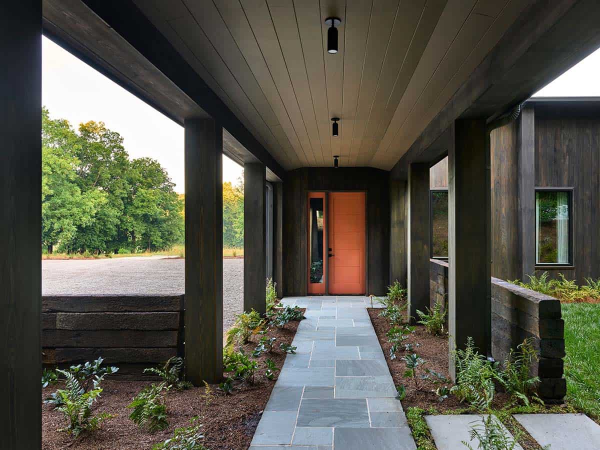 Covered entry walkway with dark wood columns leading to terracotta-painted front door