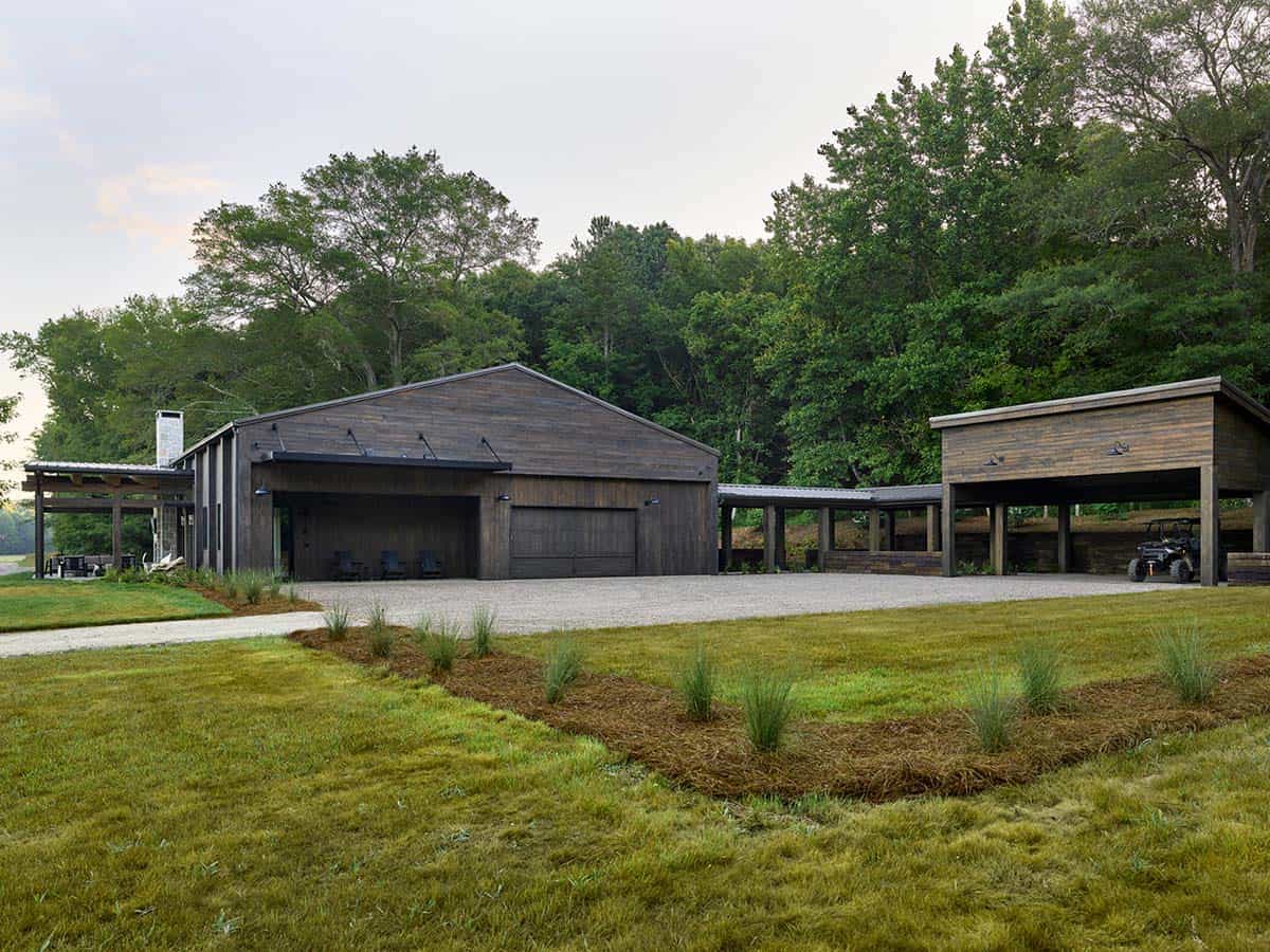 Wide exterior view of dark wood barn home with carport and open meadow at dusk
