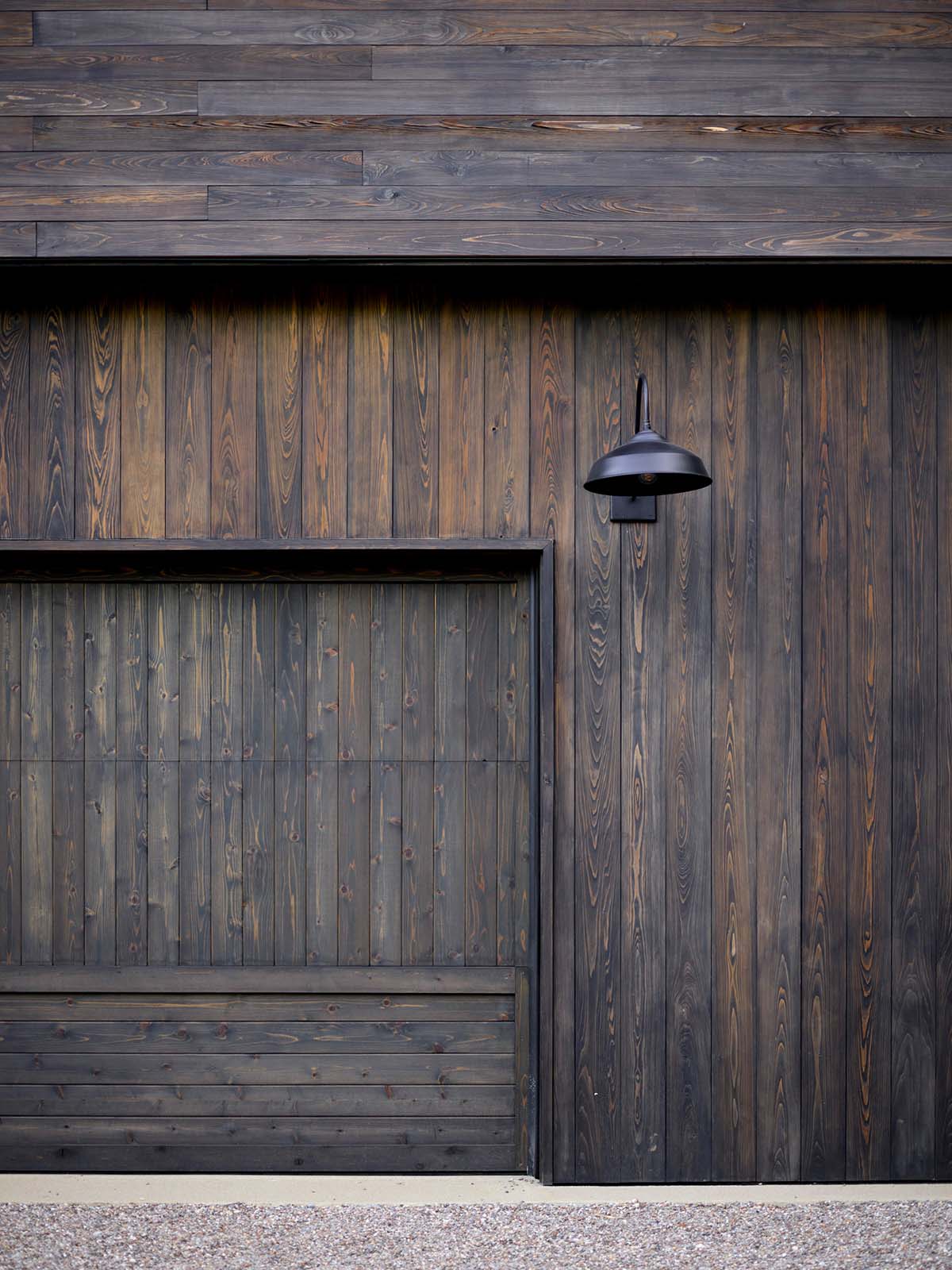 Close-up of dark stained wood garage door and vertical board siding with black gooseneck light
