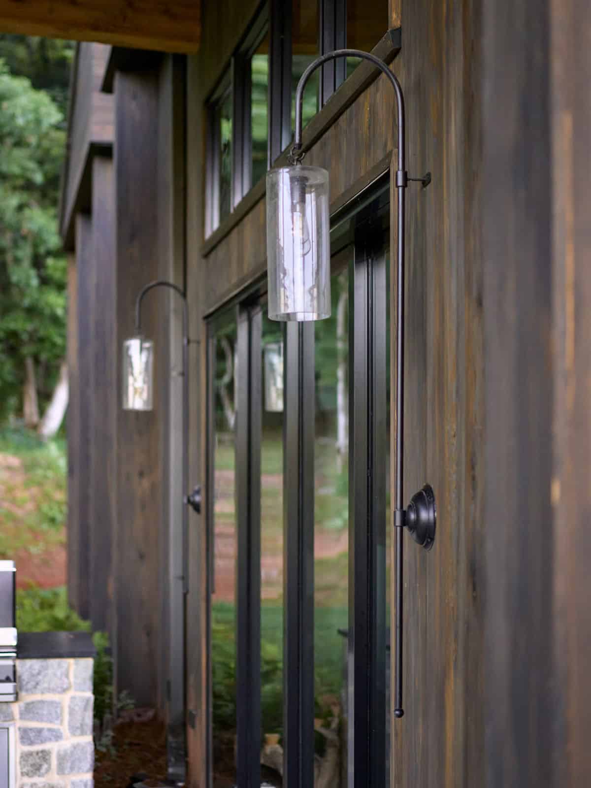 Black iron hook sconce with seeded glass cylinder shade mounted on dark wood siding