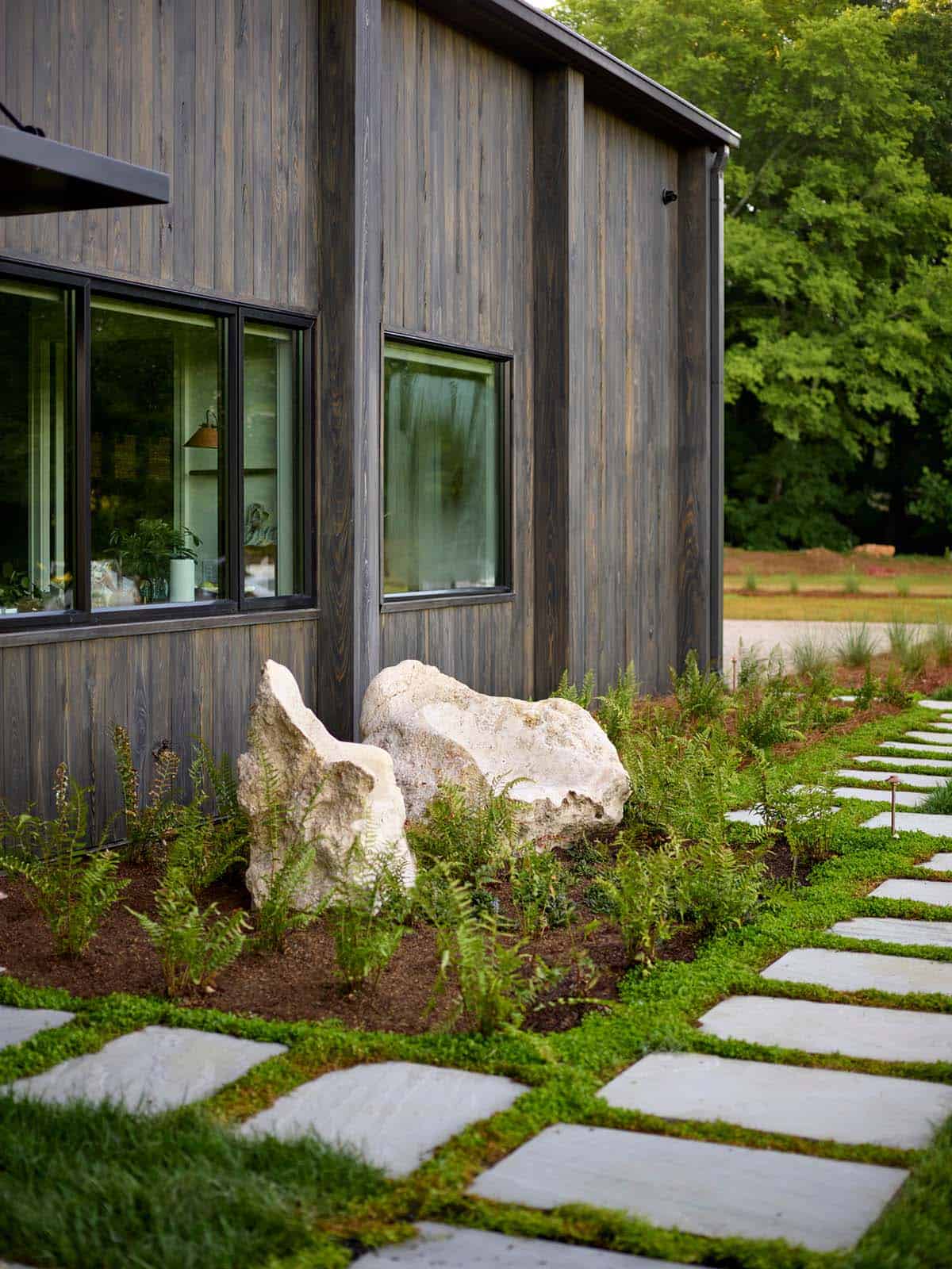 White limestone boulders and fern plantings along dark wood siding with stepping stone path