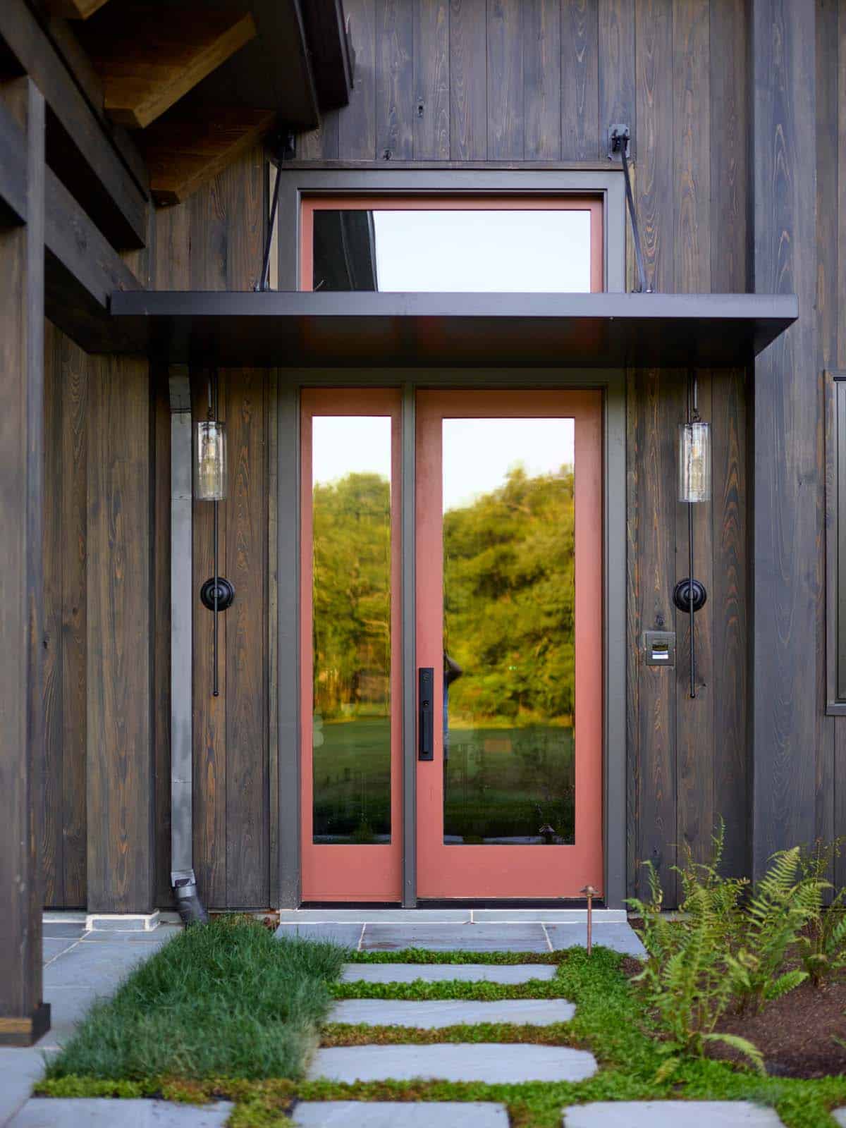 Terracotta double glass entry doors flanked by seeded glass sconces on dark wood exterior