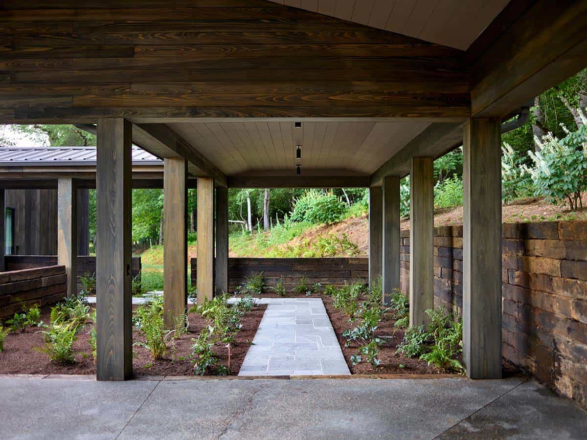 Covered walkway with wood columns framing bluestone path through planted garden beds