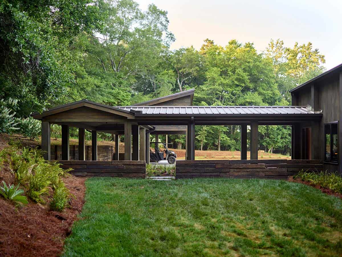 Open wood carport with metal roof, railroad tie retaining walls, and UTV, set in green lawn