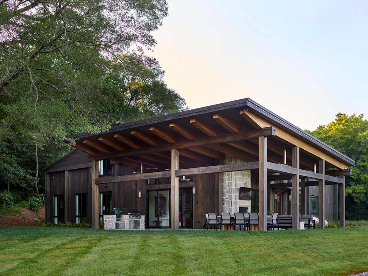 Large covered back porch with exposed wood rafters, stone fireplace, outdoor dining, and kitchen