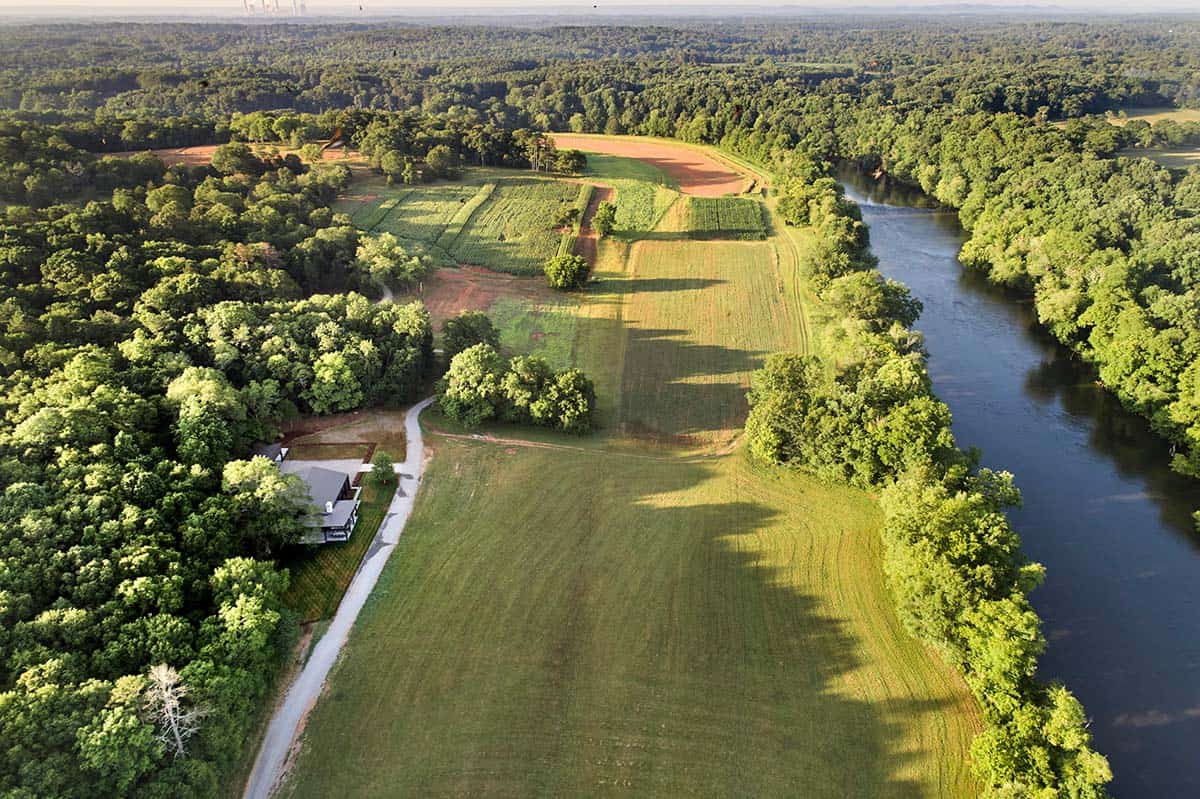 Aerial view of home and gravel driveway alongside farmland fields and winding river