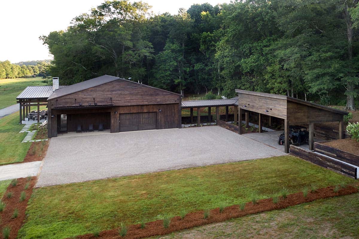 Aerial view of weathered wood barn home, carport, and gravel courtyard surrounded by trees