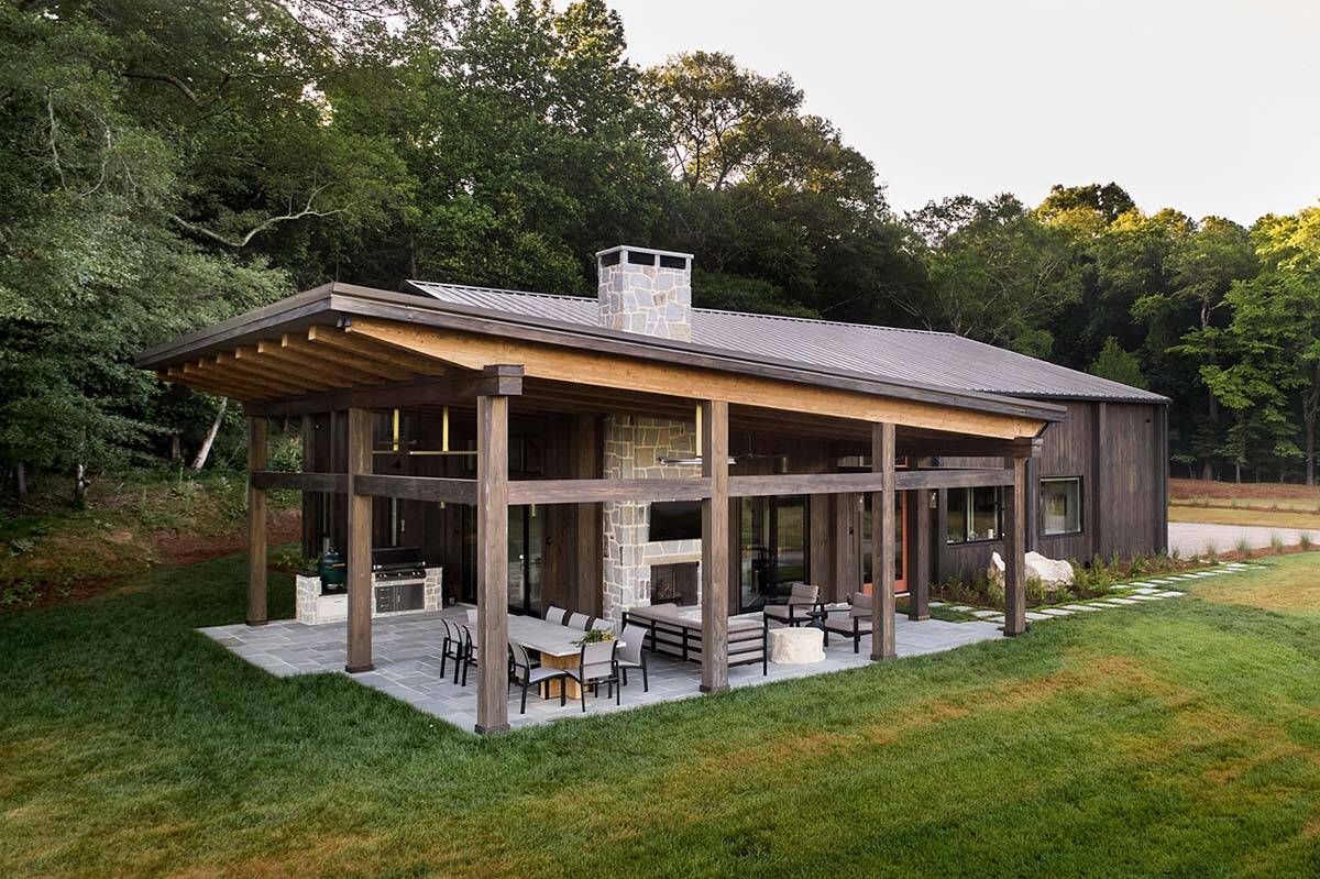 Back exterior with large covered porch, stone fireplace, outdoor dining set, and wood beam roof