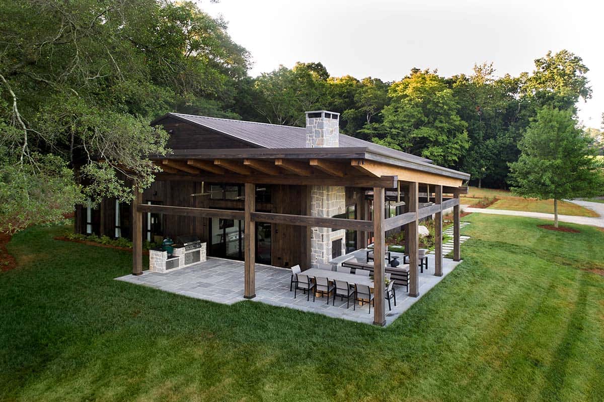 Rear aerial view of covered patio with outdoor kitchen, stone chimney, and dining area