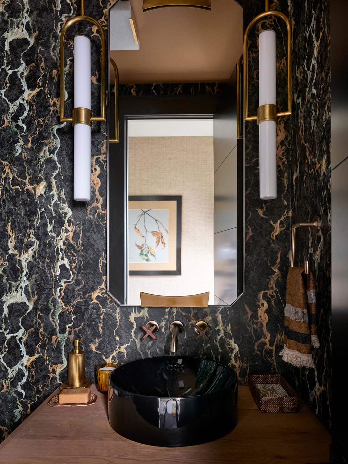 Powder room with dark green marble walls, black vessel sink, brass sconces, and brass faucet