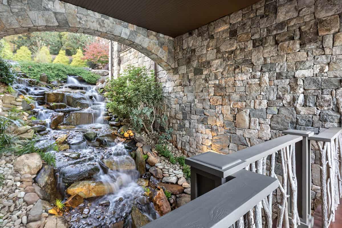 Covered porch overlooking a multi-tiered stone waterfall feature with natural landscaping