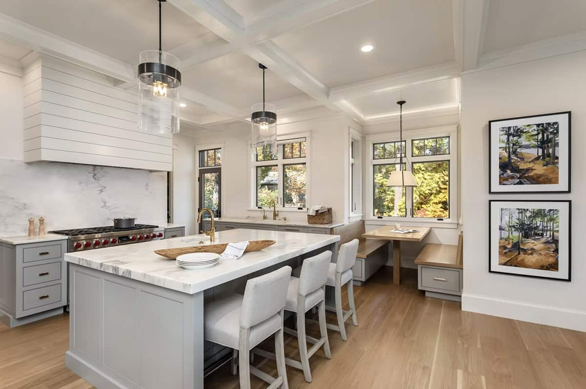 Contemporary kitchen with gray island, marble countertops, coffered ceiling, and built-in breakfast nook
